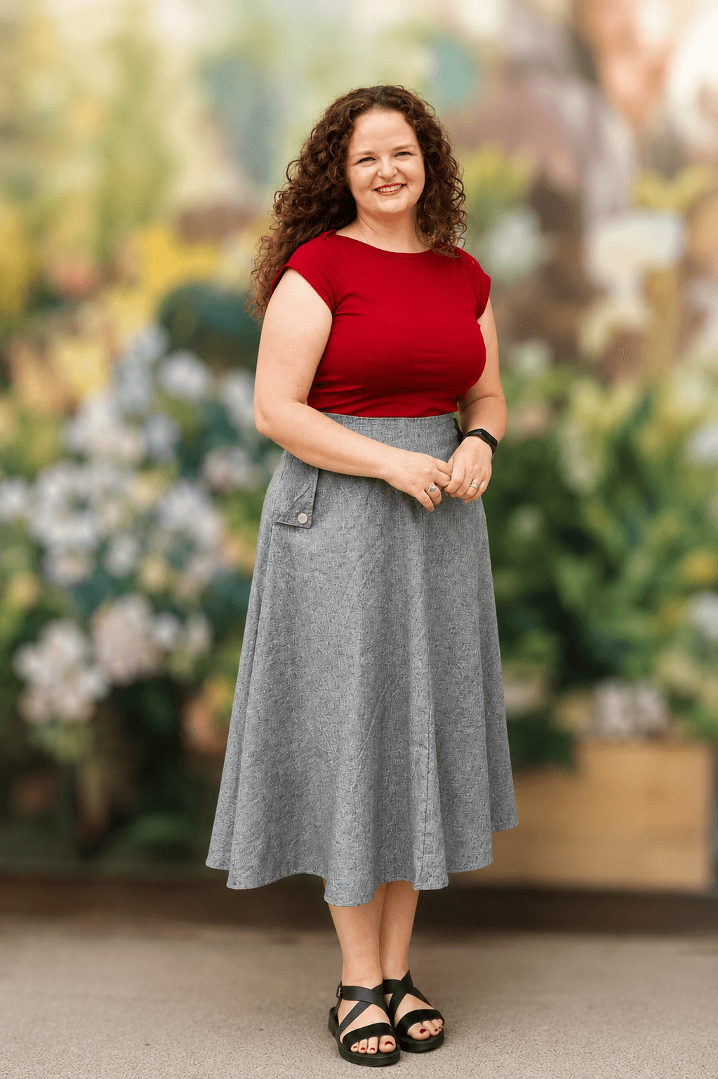 Abilene Caride standing in a red top and grey skirt against a softly blurred organic background